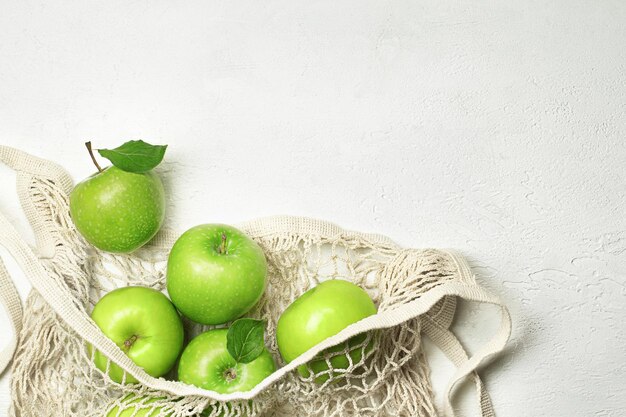 Verse groene appels in een netzakje op een licht betonnen tafelblad