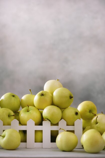 Verse groene appels in houten kist op lichtgrijs.