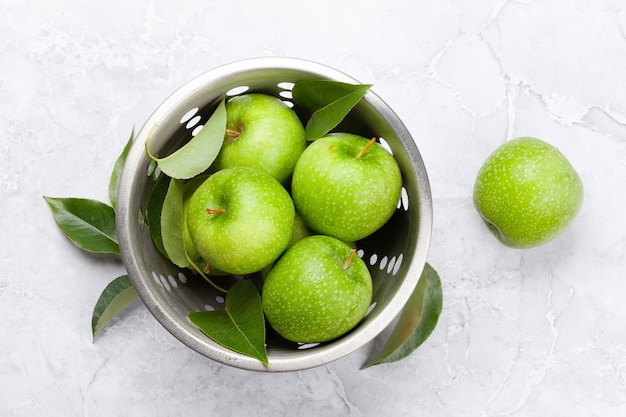 Verse groene appels in vergiet op stenen tafel