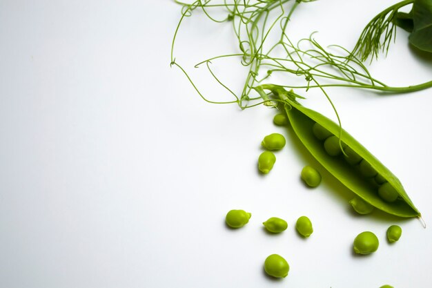 Verse groene erwtenpeulen met gebladerte op een witte achtergrond één peul is open erwten zijn zichtbaar