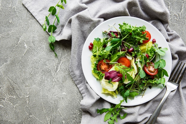 Verse groene gemengde slakom met tomaten en microgreens op concrete lijst. Gezond eten, bovenaanzicht.