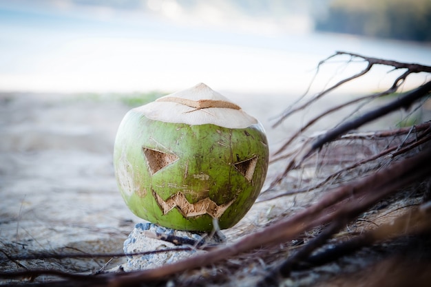 Verse groene kokosnoot is een symbool van halloween met een gesneden gezicht op pompoen ligt in wortels op het strand