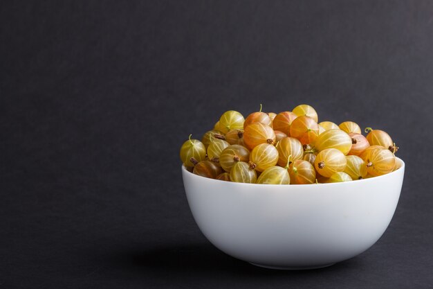 Verse groene kruisbes in witte kom op zwarte achtergrond