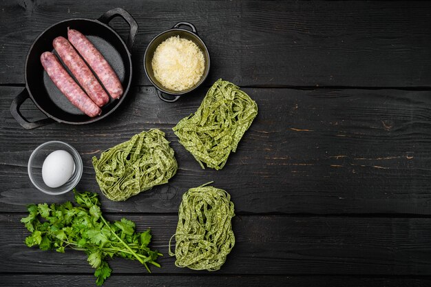 Verse groene pasta en worstjes set, op zwarte houten tafel achtergrond, bovenaanzicht plat lag, met kopieerruimte voor tekst