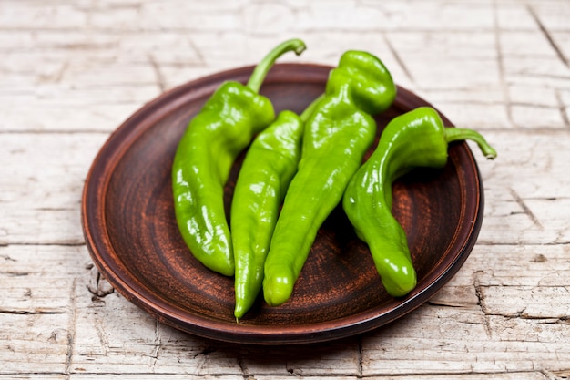 Verse groene rauwe paprika&#39;s op bruin keramische plaat op rustieke houten tafel achtergrond.