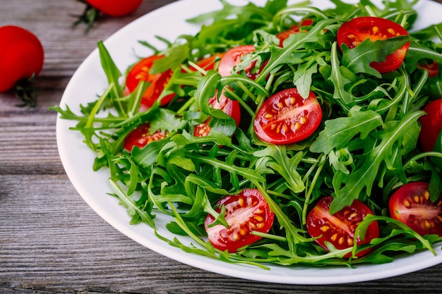 Verse groene salade met rucola en rode tomaten op rustieke houten achtergrond