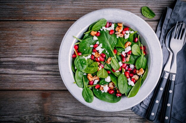 Verse groene salade met spinazie, walnoten, fetakaas en granaatappel op houten achtergrond