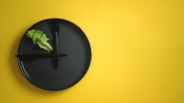 Verse groene slablad op een zwarte plaat met vork en mes dat lijkt op een klok