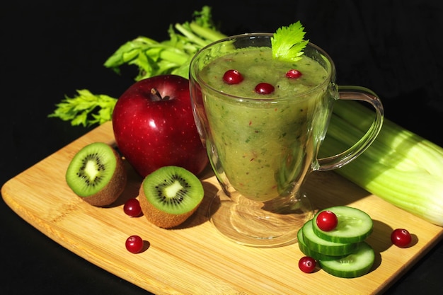 Verse groene smoothie in een glazen beker met selderij, appel, komkommer, kiwi en veenbessen, gezonde veganistische drank
