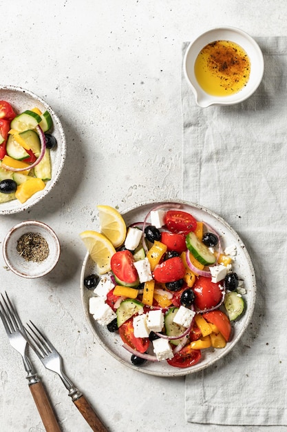 Verse groente Griekse salade met feta kaas tomaten rode ui komkommer peper olijfolie en italiaanse kruiden geserveerd op een licht getextureerde tafel met bestek Bovenaanzicht