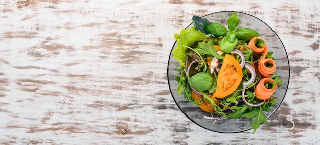 Verse Groente Salade. Rucola, tomaten, wortelen, uien. Op een houten achtergrond. Bovenaanzicht. Ruimte kopiëren.