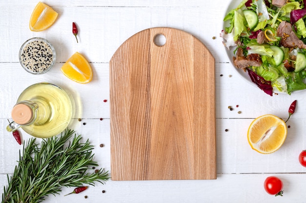 Verse groenten en ingrediënten voor het koken op witte houten achtergrond. Mockup met lege houten snijplank. Vegetarisch en gezond eten concept.