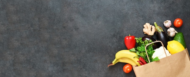 Verse groenten, fruit en greens in ambachtelijke papieren boodschappentas op zwarte rustieke achtergrond. Eco winkelen en eten levering concept.