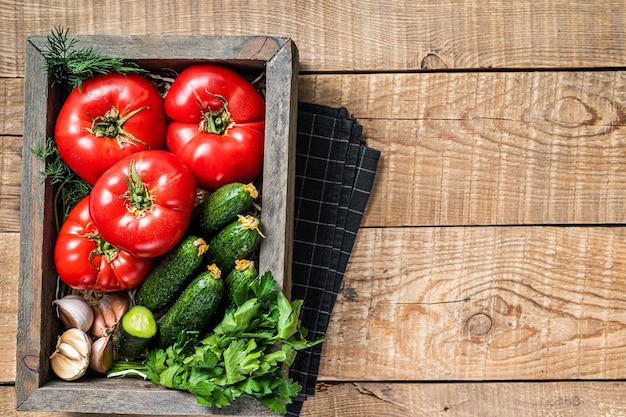 Verse groenten in een houten kist, rode tomaten, groene komkommers met kruiden. houten achtergrond. bovenaanzicht. ruimte kopiëren.