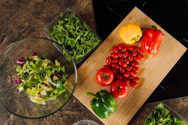 Verse groenten op houten snijplank. tomaten, paprika's, rucola ingrediënten voor salade. veganisme gezond voedselconcept en bovenaanzicht.
