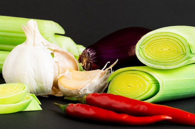 Foto verse groenten op zwarte achtergrond: selderij, prei, rode ui, chili peper en knoflook.