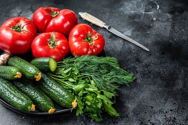 Verse groenten voor zomer groene salade, rode tomaten, komkommers, peterselie, kruiden. Zwarte achtergrond. Bovenaanzicht. Ruimte kopiëren.