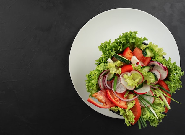 Verse groentesalade in een zwarte kop op een grijze schotel. Uitzicht van boven.