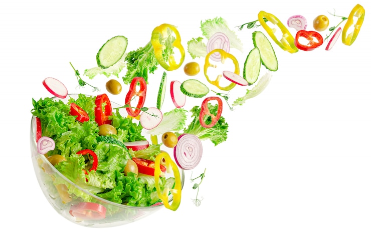 Foto verse groentesalade in transparante kom met vliegende ingrediënten die op wit worden geïsoleerd. gezond eten concept.