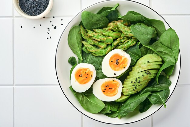 Verse groentesalade met avocado, asperges, gekookte eieren op wit betegeld oppervlak. Bovenaanzicht.