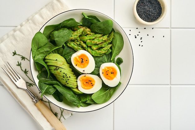 verse groentesalade met avocado asperges verfrommelde eieren zwarte sesamzaadjes en spinazie op bord