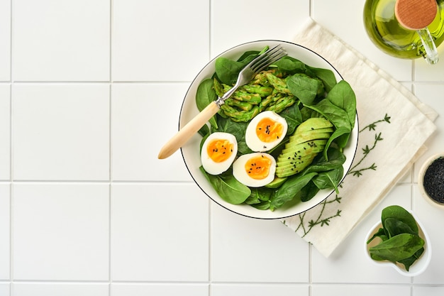 verse groentesalade met avocado asperges verfrommelde eieren zwarte sesamzaadjes en spinazie op bord