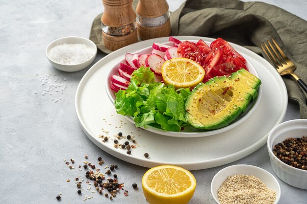 Verse, groentesalade met avocado op een bord met citroen, peper en zout op een grijze achtergrond