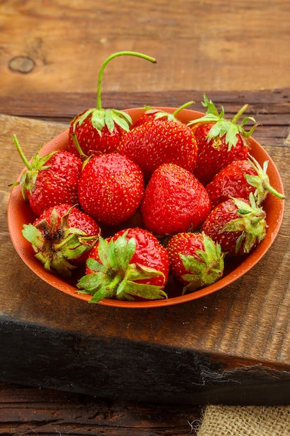 Verse grote aardbeien in een kleiplaat op een houten tafel op een standaard. Verticale foto