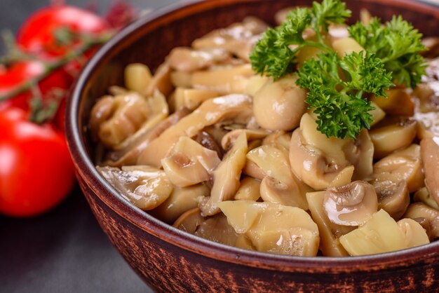 Verse heerlijke pittige ingeblikte champignons met kruiden en specerijen in keramische gerechten op een donkere betonnen achtergrond
