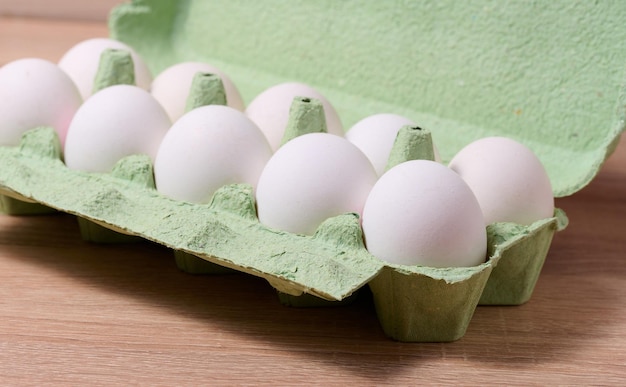 Verse hele witte eieren in groene papieren verpakkingen op een houten tafel