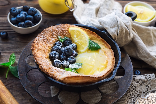 Verse huisgemaakte Nederlandse baby pannenkoek met lemon curd en bosbessen in ijzeren koekepan op rustieke houten.