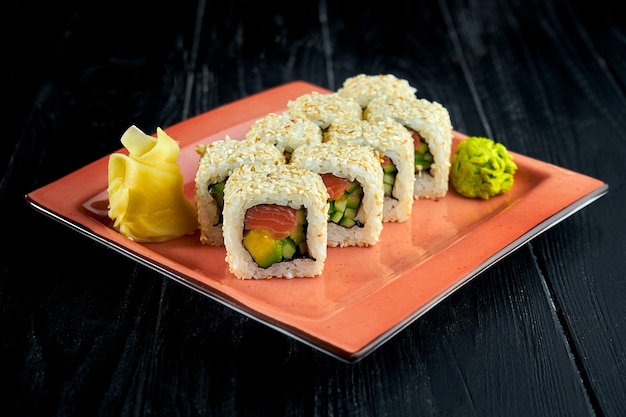 Verse, Japanse sushibroodjes met avocado, komkommer en zalm, geserveerd in een bord met wasabi en gember op een donkere achtergrond.