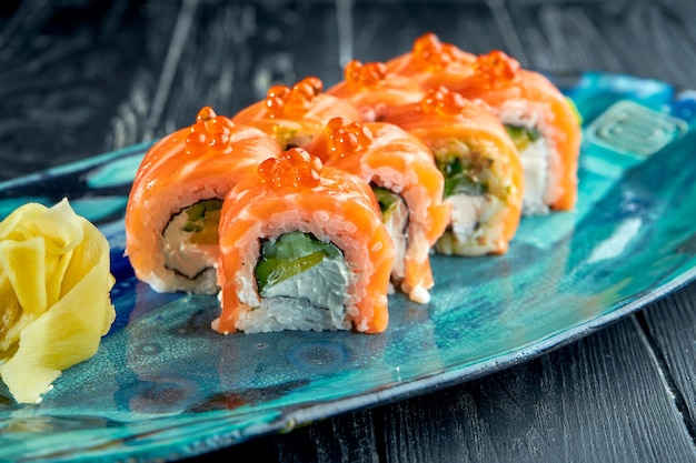 Verse, Japanse sushirolletjes met komkommer, kaviaar en zalm, geserveerd in een bord met wasabi en gember op een donkere ondergrond. Japanse keuken. Rode drakenrol in sesam