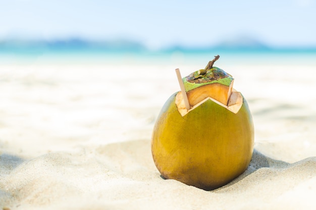 Verse jonge kokosnoot liggend op het zandstrand met stro klaar voor drank