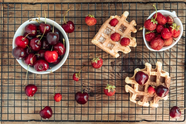 Verse kersen in een kom en aardbeien met Weense wafels op een houten tafelblad