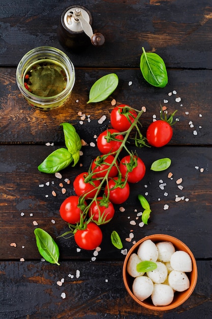 Verse kerstomaten, basilicumbladeren, mozzarella kaas en olijfolie op oude houten ondergrond. Caprese salade ingrediënten. Selectieve aandacht.