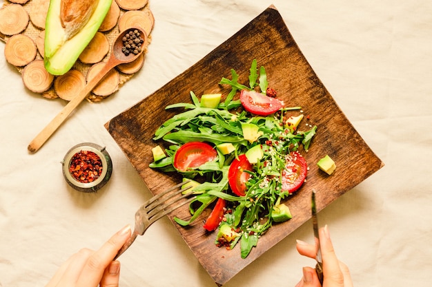 Verse lichtgroene salade met avocado en tomaten in een houten plaat.