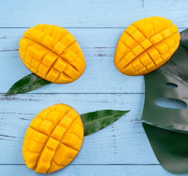 Verse mango mooi gehakt fruit met groene bladeren op helder blauwe hout achtergrond Tropisch fruit ontwerpconcept Plat lag Bovenaanzicht Kopieer ruimte