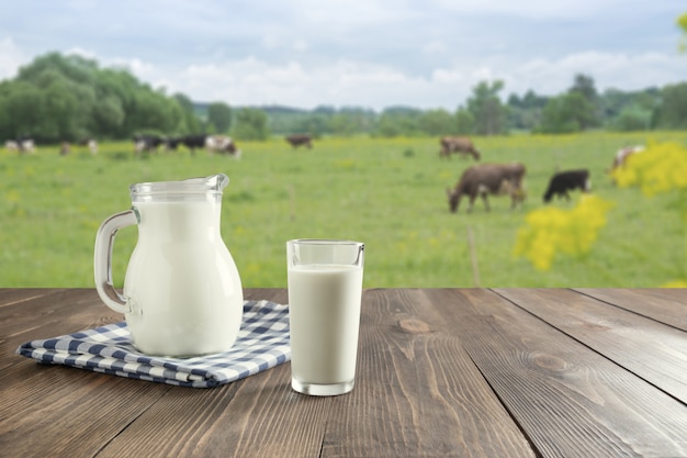 Foto verse melk in glas op donkere houten tafel en wazig landschap met koe op weide. gezond eten. rustieke stijl.