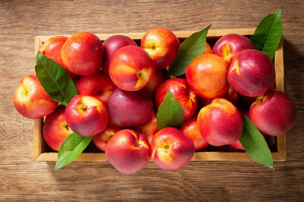 Verse nectarines met bladeren in een houten kist bovenaanzicht