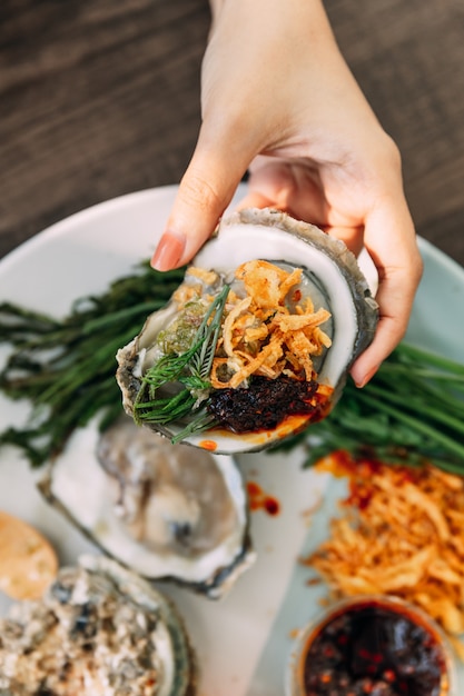 Verse oester in de hand in de hand die bedekt met gebakken sjalot, chilipasta, Acacia Pennata en Thaise vissaus.