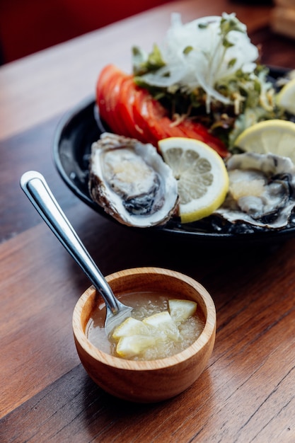 Verse oesters close-up op zwarte plaat, geserveerd tafel met oesters, citroen, ijs en salade.