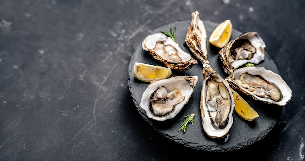 Verse oesters met citroen geserveerd op ronde schotel geïsoleerd op zwart oppervlak