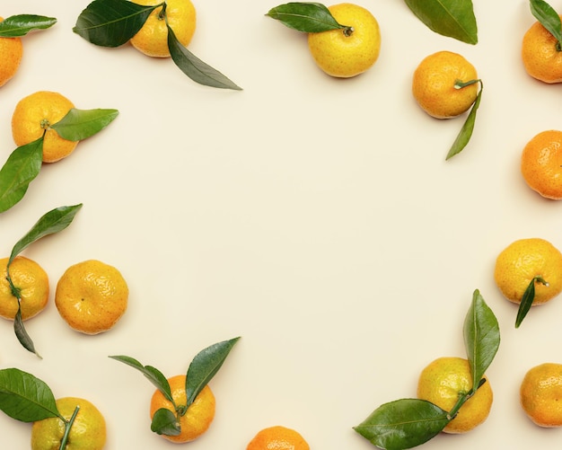 Verse oranje gele mandarijnen met groene bladeren op beige tafel rond frame met kopieerruimte
