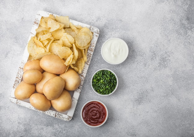 Verse organische eigengemaakte chips met ruwe gele aardappels in wit houten vakje op lichte lijstachtergrond.