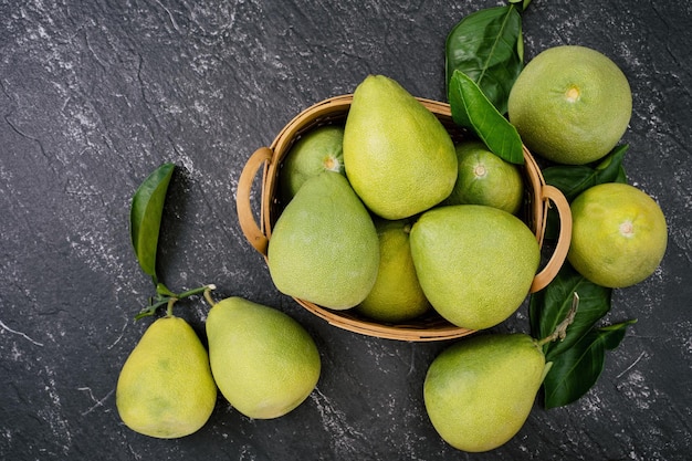 Verse pomelo pummelo grapefruit shaddock in bamboe mand met blad op donkere zwarte leisteen achtergrond Seizoensgebonden fruit concept bovenaanzicht plat lag