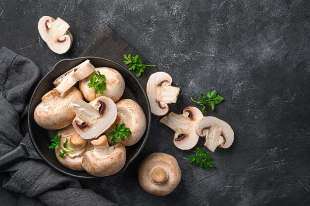 Verse, rauwe champignons met peterselie in een koekenpan op een zwarte achtergrond. Bovenaanzicht, horizontaal. Champignons koken.