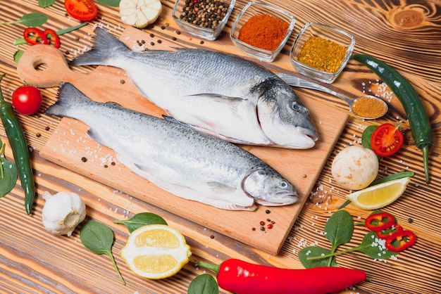 Verse rauwe dorado vis. zeebrasem, liggend op een houten bord op een tafel met kruiden en zout en specerijen. dorado en ingrediënten voor het koken op tafel. detailopname