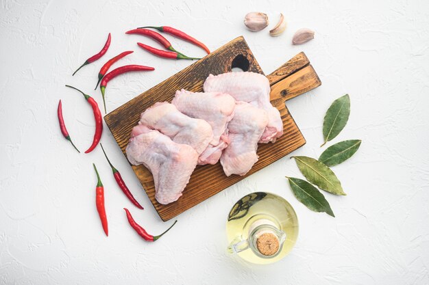 Verse rauwe middelste kippenvleugels met ingrediënten ingesteld, op houten snijplank, op witte tafel, bovenaanzicht plat lag