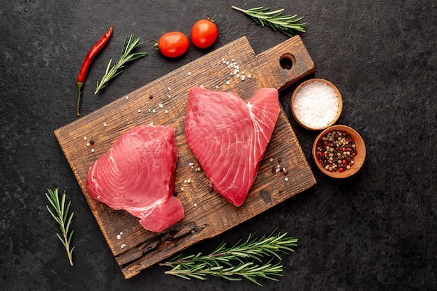 Verse rauwe tonijnlapjes vlees met rozemarijn en kruiden op een stenen achtergrond